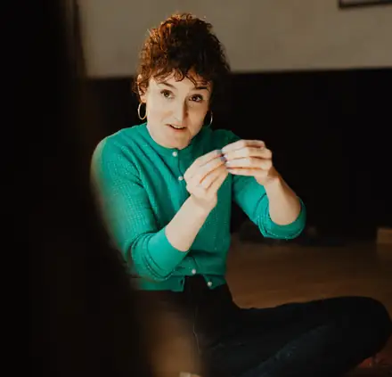 Ángela Palacios, sentada y explicando con las manos, da clase a un grupo en una sala con luz natural.